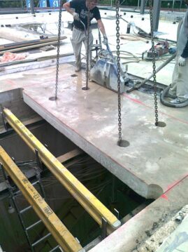 Bauarbeiter hebt Betonteile mit Ketten über einer Baustelle mit einem offenen Bereich.