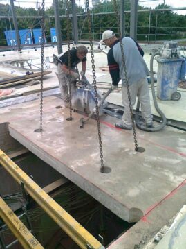 Zwei Bauarbeiter, die an einer Betonplatte auf einer Baustelle arbeiten, mit Werkzeugen und Maschinen.