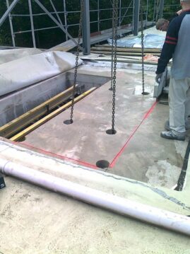Betonplatte mit markierten Löchern und Hebezeugen auf einer Baustelle.