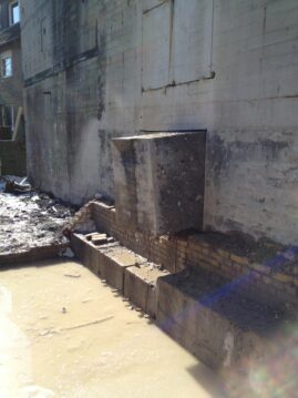 Ein Betonblock, der an einer Wand steht, umgeben von Wasser und Schmutz.
