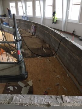 Unvollendeter Innenraum mit freiliegenden Holz- und Betonoberflächen sowie Baugeräten.