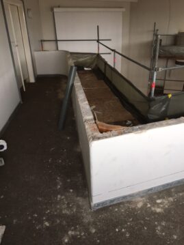 Ein Raum im Umbau mit einer halbhohen Wand und Baustellenmaterialien sichtbar.