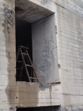 Ein Baugerüst steht neben einem rechteckigen Fenster in einer Betonwand während der Bauarbeiten.