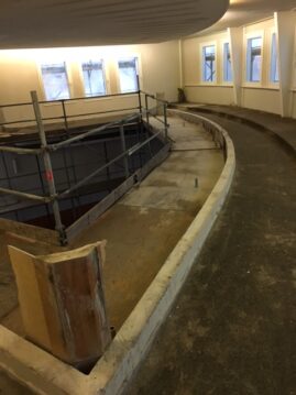 Bauarbeiten an einer geschwungenen Wand mit Gerüst und unvollendeter Oberfläche.