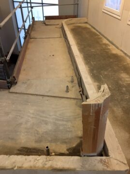 Unfertige Betonfläche mit Holzrahmen und Rohren während der Bauarbeiten in einem Innenraum.