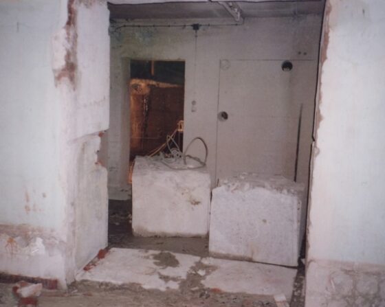 Innenraum mit zwei großen, rechteckigen Betonblöcken auf dem Boden und einer Tür im Hintergrund.